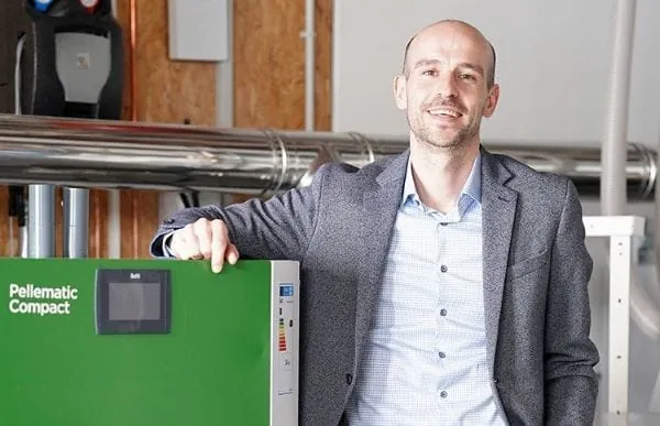 Vertriebsleiter von ÖkoFen Deutschland, Aaron Ehinger lehnt auf einem grünen Pelletskessel. Pellematic Compact