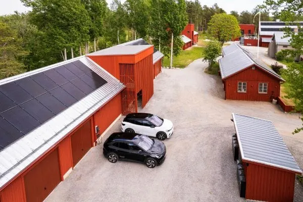 Öko-Hof mit roten, schwedischen Holzhäusern und E-Autos vor der Garage