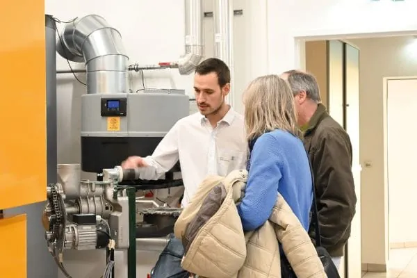 KWB-Mitarbeiter zeigt zwei G&auml;sten (Mann und Frau) einen Hackgutkessel auf der Hausmesse