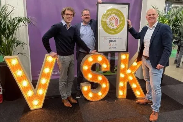 Gerahmtes Europäisches Gütesiegel für Infrarotheizungen halten die Das neue Gütesiegel für Infrarotheizungen wurde auf der Messe VSK im Februar in den Niederlanden erstmals vorgestellt. Auf dem Bild: Casper Esmeijer (Peutz), Remi Hompe (Stichting Binnenklimaattechniek) und Bas Spekreijse (European Infrared Heating Alliance EIHA) (v. l.).erantwortlichen der Fachverbände hoch. Sie stehen an den Leuchtbuchstaben der Messe VSK in den Niederlanden.