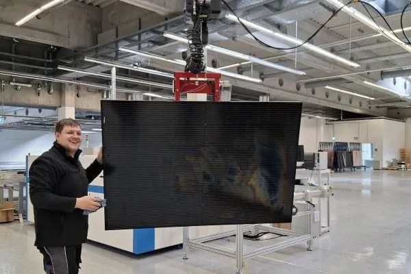 Sunmaxx-Mitarbeiter kontrolliert PVT-Modul, das am Roboterarm h&auml;ngt.