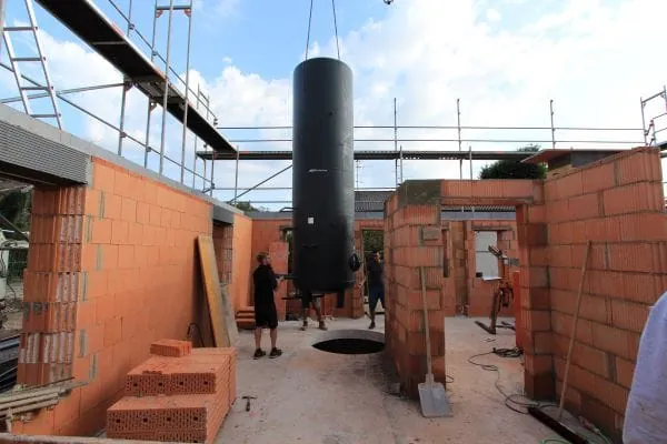 Rohbau eines Sonnenhauses. Der gro&szlig;e Pufferspeicher wird per Kran ins Geb&auml;ude eingebracht.