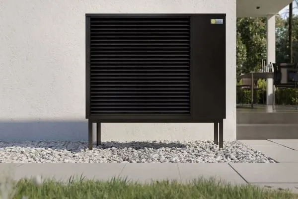 Luft-/Wasser-Wärmepumpe schwarz steht an Außenwand im Garten.