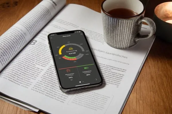 Tasse Kaffee und Smartphone auf einer Zeitschrift. Handydisplay zeigt Photovoltaikstromrechner von Buderus.