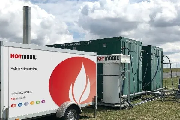 mobile Heizzentrale von Hotmobil auf Autoanh&auml;nger vor zwei dunkelgr&uuml;nen mobilen Duschcontainern der eSKa GmbH auf gr&uuml;ner Festivalwiese