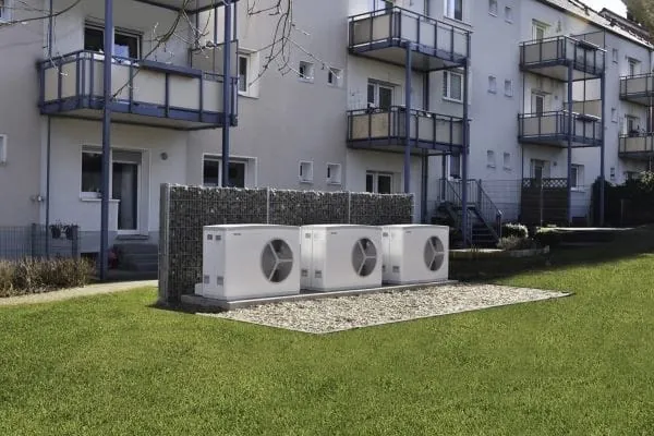 3 wei&szlig;e W&auml;rmepumpen in Monoblockbauweise vor Mehrfamilienhaus