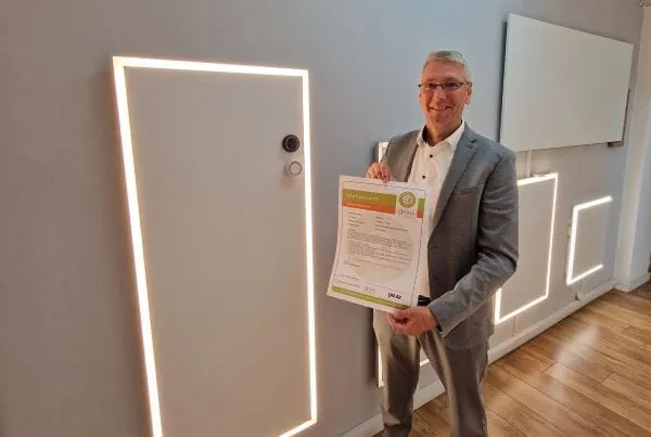 Gesch&auml;ftsf&uuml;hrer Uwe Lucht mit G&uuml;tesiegel f&uuml;r Infrarotheizungen in den H&auml;nden im Ausstellungsraum mit Infrarotheizungen an der Wand