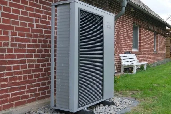 Monoblock-&auml;rmepumpe mit grauer Verkleidung vor Einfamilienhaus-Bungalow mit kassandraroter Klinkerfassade