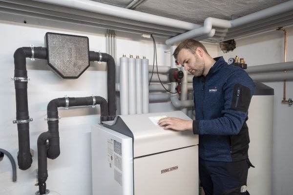 Heizungsbauer steht vor Wärmepumpen-Inneneinheit im Heizungskeller