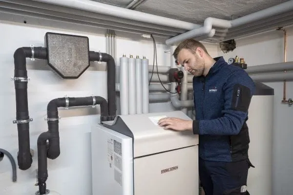 Heizungsbauer steht vor Wärmepumpen-Inneneinheit im Heizungskeller