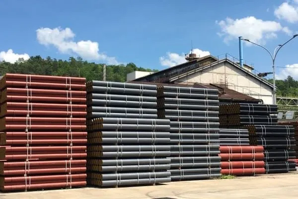 Gusseiserne Abwasser-Rohre aufgestapelt auf einem Freigel&auml;nde. Sonniges Wetter und Sch&auml;fchenwolken.
