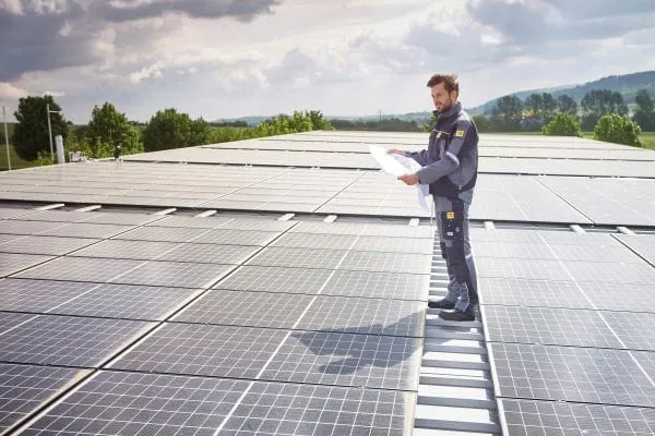 Elektroniker steht mit Plan auf Photovoltaik-Anlage