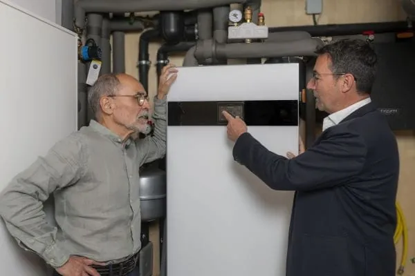 W&auml;rmepumpenbetreiber und Energieberater vor Inneneinheit im Heizungskeller.