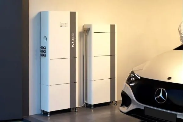 Stapelbares Batteriespeicher-System steht vor der Wand einer Garage. Davor E-Auto.