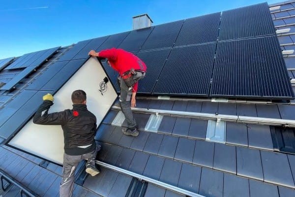 zwei Solarteure montieren PV-Module auf ein Dach.
