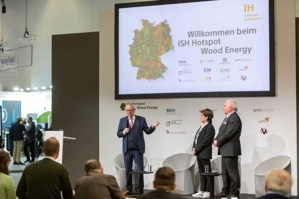 Areal in Halle 11 mit Hotspot Holzw&auml;rme. 3 Branchenvertreter auf dem Podium stellen vor Publikum die Initiative Holzw&auml;rme vor. Bild von ISH 2023