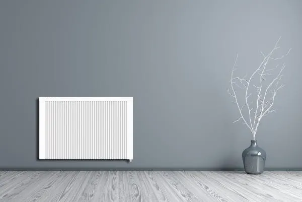 wei&szlig;er Elektro-Heizk&ouml;rper vor grauer Wand. Daneben eine Bodenvase mit wei&szlig;en &Auml;sten