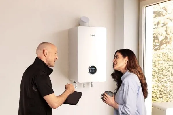 Heizungsinstallateur und Kundin vor wandhängenden Hybridheizgerät (Wärmepumpe/Erdgas)