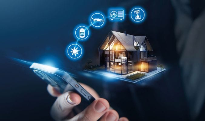 Grafik mit beleuchteten gläsernen E-Haus vor dunkelblauem Hintergrund. 5 runde Grafiken mit Symbolen für Sonne, Stromspeicher, E-Auto, Wärmepumpe und Handy-App. Im Vordergrund Hand mit Smartphone.