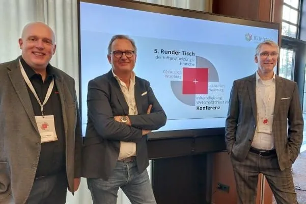 Drei M&auml;nner in Anzug vor Bildschirm mit Pr&auml;sentation auf der Konferenz.