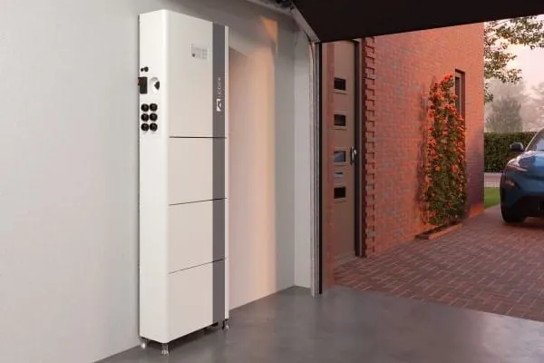 Stromspeicher aus stabelbaren Modulen steht an der Wand einer Garage. Im Hintergrund geöffnetes Garagentor mit davor parkenden E-Auto.