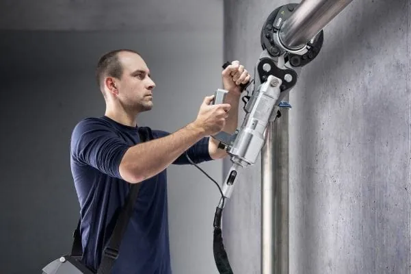 Installateur mit Presswerkzeug vor Edelstahl-Rohrleitung