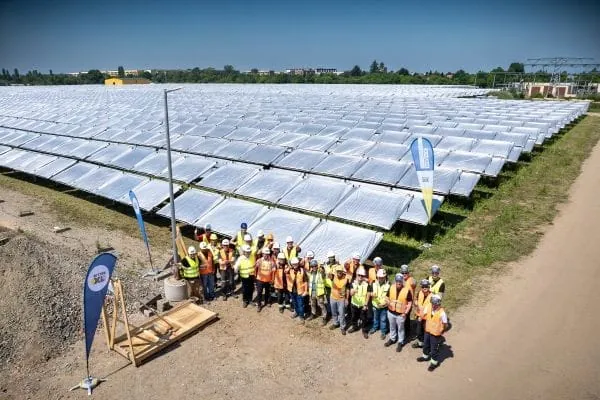 Aufnahme von oben: Projektbeteiligte sthen mit neongelben und orangen Westen vor dem mit Planen abgdeckten Solarthermie-Kollektorfeld der Stadtwerke Leipzig im Stadtteil Gr&uuml;nau. Alle tragen Schutzhelme.