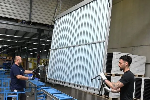 Zwei Mitarbeiter bereiten einen in der Wekhalle an Stahlseilen hrabh&auml;ngenden Gro&szlig;kollektor mit Vakuumr&ouml;hren zum Transport vor