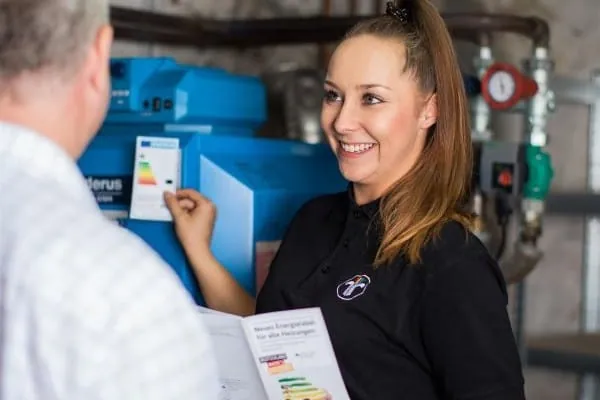 Schornsteinfegerin ber&auml;t Heizungsbesitzer vor &Ouml;lheizkessel im Heizungskeller &uuml;ber Energieverbrauch