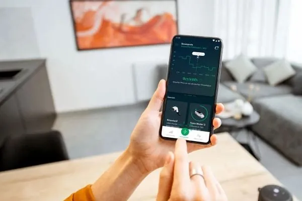 Frauenhände halten Smartphone mit Bildschirmanzeige Rabot Energy App. Im Hintergrund Wohnzimmer.