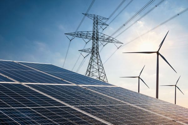 PV-Freiflächenanlage mit aufgeständerten Modulen. Im Hintergrund Strommast mit Überlandleitungen und Windräder.