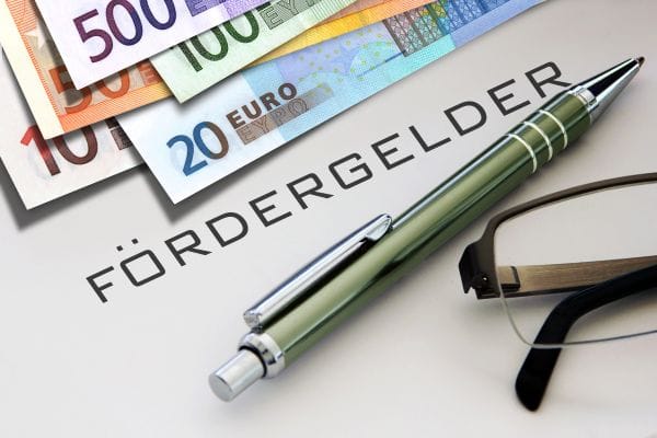 Symbolfoto mit Geldscheinen, Schrift "Fördergelder", Kugelschreiber und Brille auf Schreibtisch