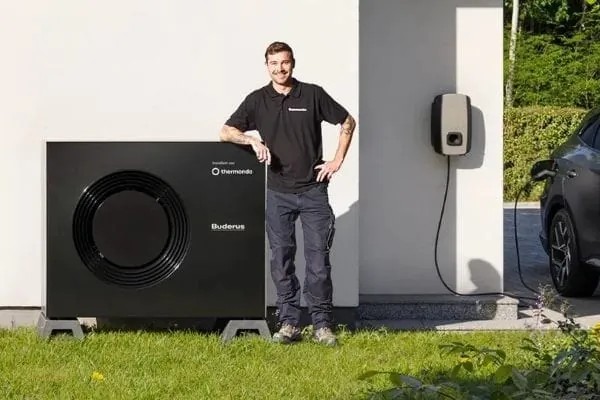 Thermondo-Installateur steht neben Monoblock-Wärmepumpe vor Haus. An der Haudwand eine Wallbox und das Kabel zum E-Auto