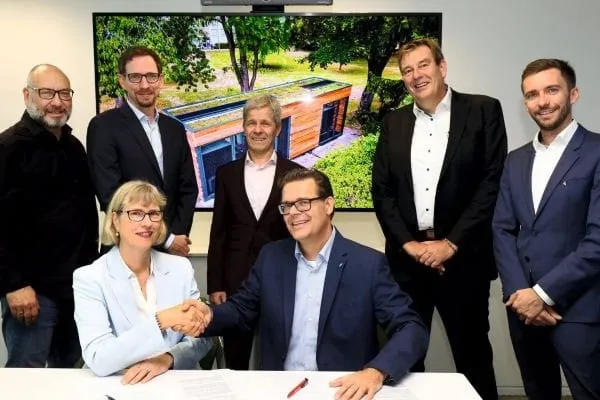 Sieben Mitarbeitende Daikin und Wohnungsunternehmen NHW bei Vertragsabschluss. Vorn reichen sich 2 sitzende Personen die Hand, die anderen stehen hinter dem Tisch