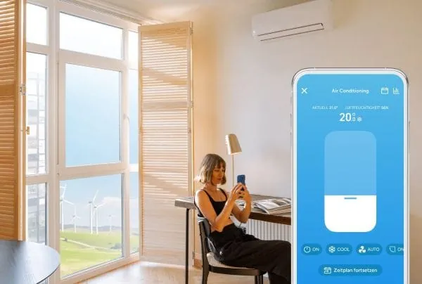 Symbolfoto: Junge Frau sitz in einem sonnendurchfluteten Raum am Schreibtisch und schaut auf ihr Smartphone mit tado-App. Im Vordergrund Handy mit hellblauer Anzeige Tado-App-Screen F