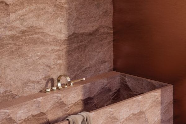 Auch an der Badewanne und in der Dusche kontrastiert die archaische Textur des Steins, dessen rohe Bruchkanten an unberührte Felsformationen erinnern, mit der Eleganz der Oberfläche Messing gebürstet (23kt Gold).