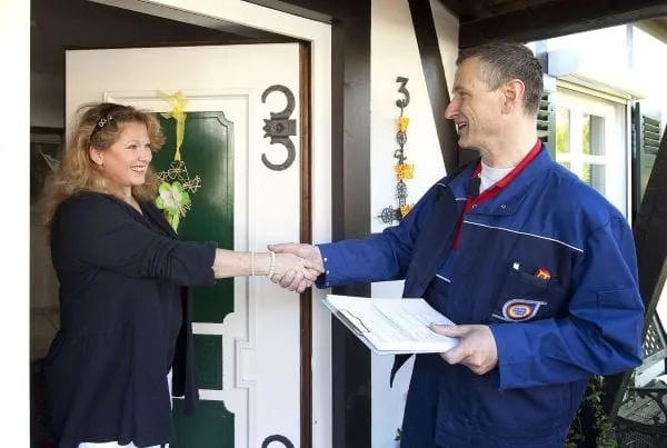 SHK-Handwerker begrüßt freundlich Kundin an der Haustür eines Einfamilienhauses