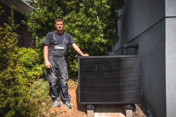 Heizungsmonteur steht neben einer Luft-/Wasserw&auml;rmepumpe am Haus des Kunden