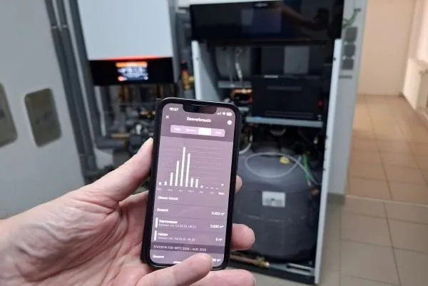 Kundenanlage HHS-Hybridbox: Kunde hält Handy mit App-Anzeige mit gesunkenen Gasverbrauch in die Kamera vor seiner Heizung im Keller