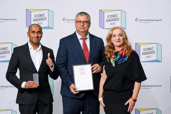 Preisverleihung Iconic Award 2025, 3 Presonen vor Fotowand, Mann in der Mitte h&auml;lt Urkunde in den H&auml;nden