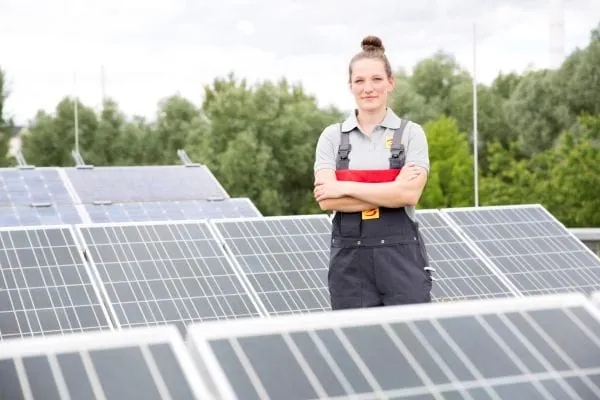 Junge Frau mit verschr&auml;nkten Armen in Arbeitskleidung Elektrikerin steht inmitten von PV-Modulen