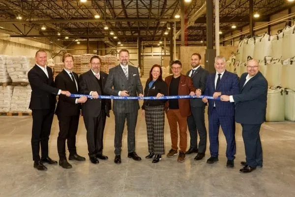 9 Personen in Anz&uuml;gen halten ein blaues Band in ihren H&auml;nden. Im Hintergrund Rohstoffe f&uuml;r die Keramikprofuktion in S&auml;cken