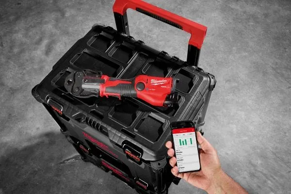 Werkzeug-Trolley mit Presswerkzeug obendrauf, eine Hand h&auml;lt ein Handy mit Anzeige der One-Key-App von Milwaukee