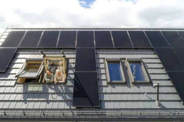 PV-Dach Reihenhaus mit 4 nebeneinander liegenden Dachfenstern. Aus einem schaut ein Ehepaar.