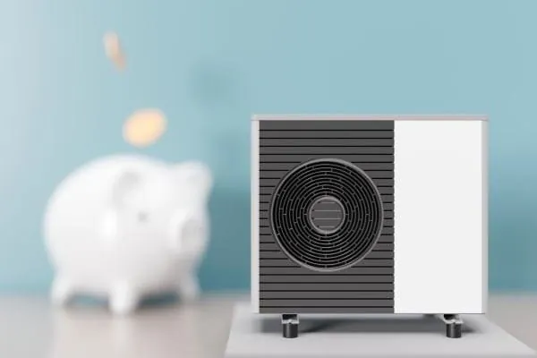 Symbolbild mit W&auml;rmepumpe im Vordergrund, dahinter verschwommen ein wei&szlig;es Sparschwein
