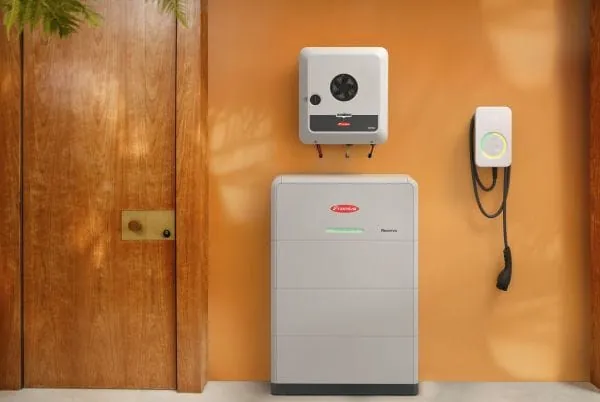 Stromspeicher, Wechselrichter und Wallbox vor einer goldbraunen Wand, von der Sonne angestrahlt