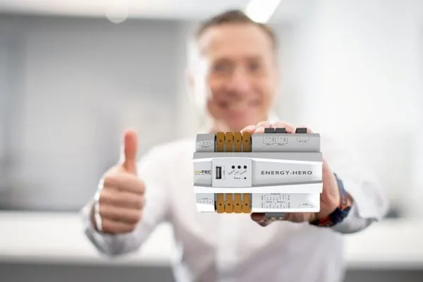 Mann, verschwommen im Hintergrund, zeigt Energy Her (Smart Meter) in die Kamera.