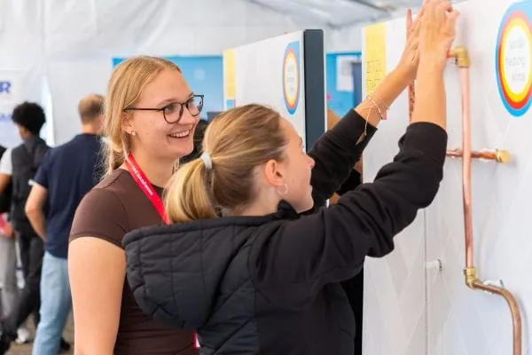 Zwei jungen Frauen an der Demo-Installationswand mit Kupferrohren