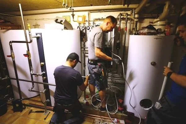 3 Heizungsinstallateure beim Einbau einer Wärmepumpenanlage, Montage der Inneneinheit im Heizungskeller
